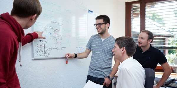 vier Personen vor einem Whiteboard