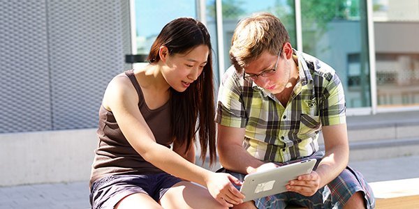 2 Studierende mit Tablet auf einer Bank vor dem Gebäude C19, Darmstadt