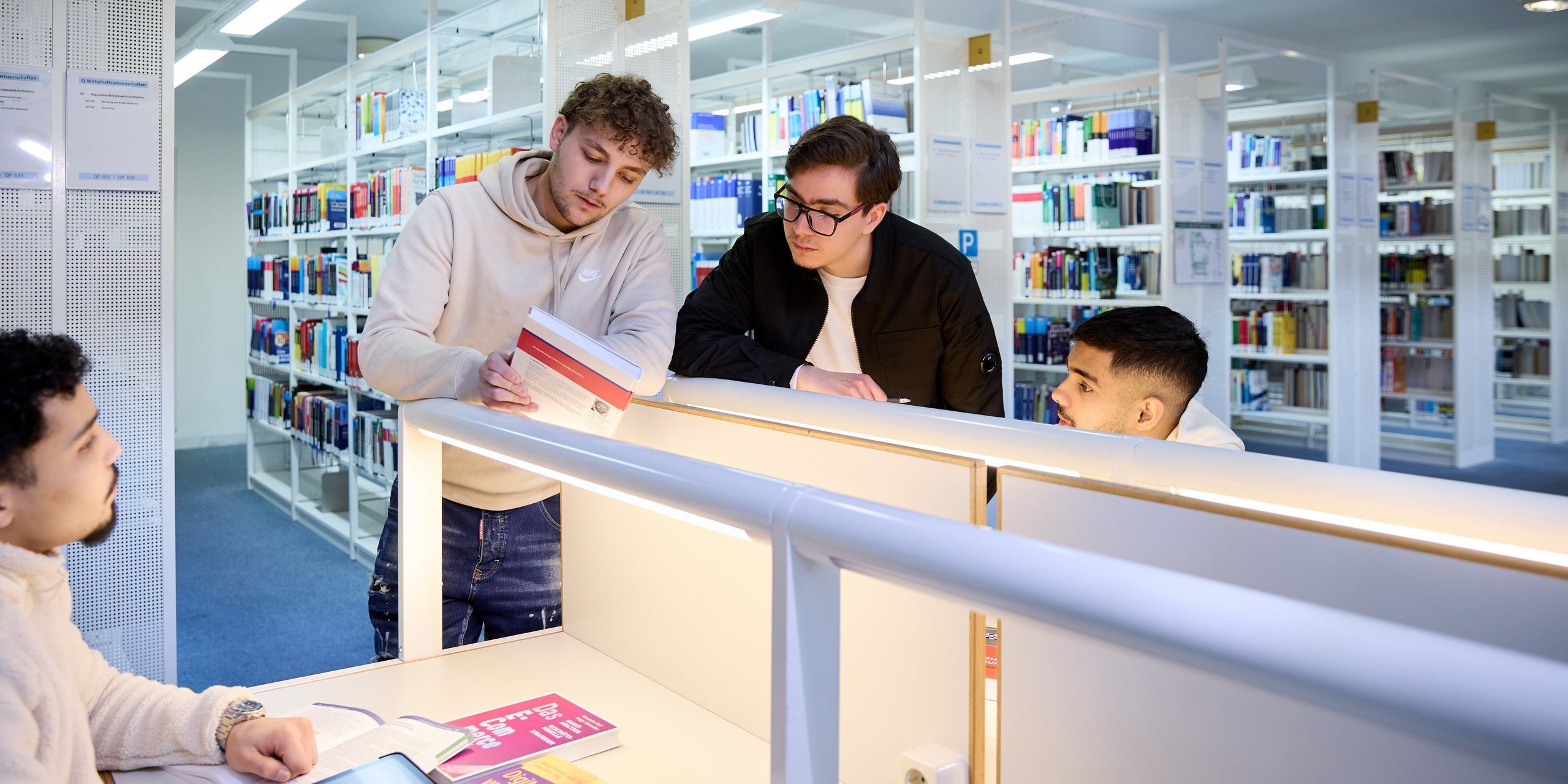 in einer Bibliothek betrachten vier Personen ein Buch