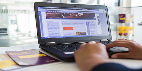Info-Flyer der h_da und ein geöffneter Laptop mit der Hochschul-Startseite