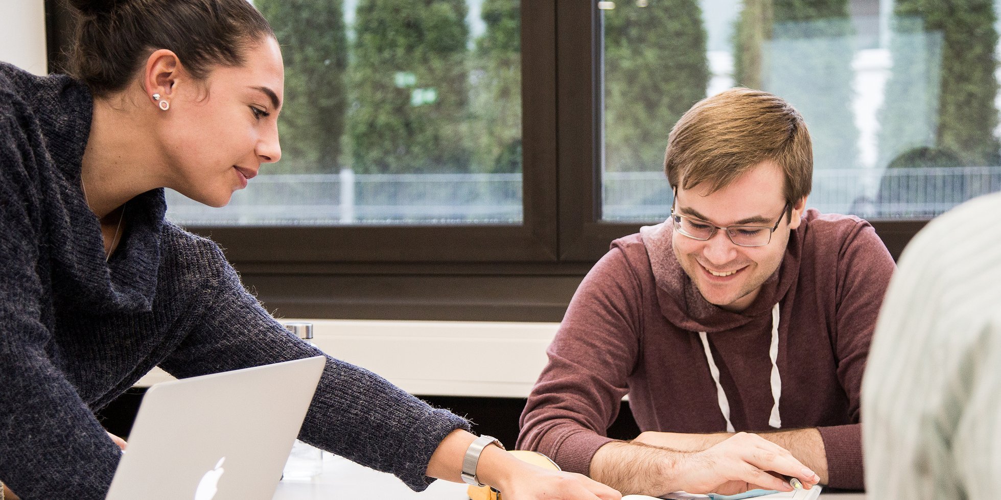 zwei Personen mit Schreibutensilien und Notebook an einem Tisch