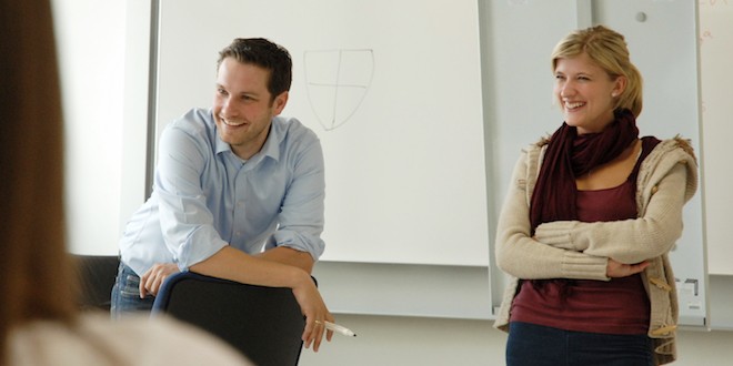Ein Trainer und eine Trainerin stehen vor einer Flipchart und unterhalten sich mit Teilnehmer*innen.