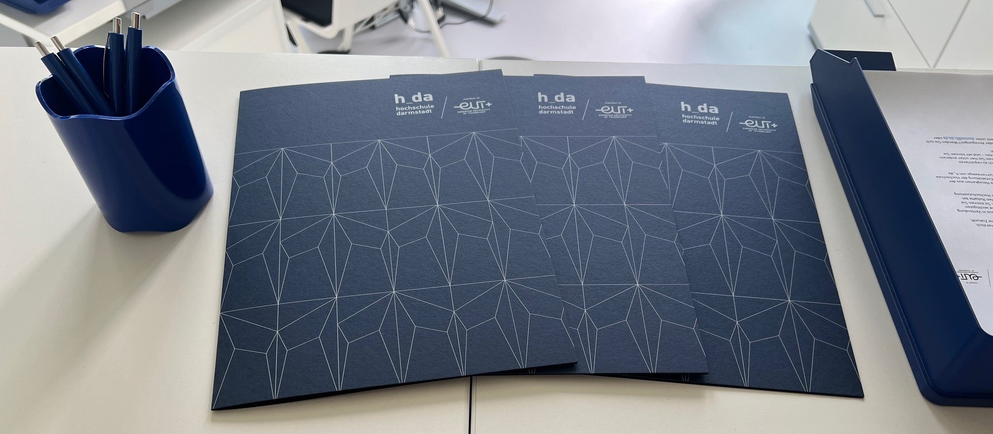 Gratulationsmappen der h_da und Stifte auf der Theke im Raum 1.20 in Gebäude C23, wo di Ausgabe der Abschlussdokumente stattfindet.