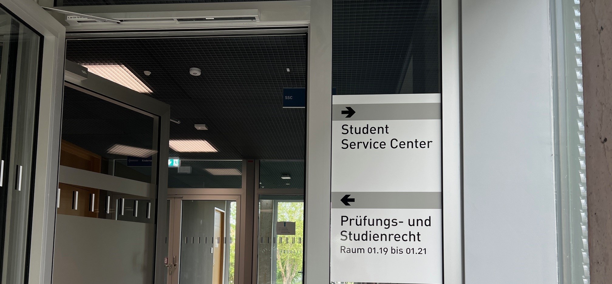 Beschilderung an der Tür am Ende des Treppenaufgangs in den 1. Stock im Gebäude C23. Rechts geht es zum Student Service Center, links zum Zentralen Prüfungsamt